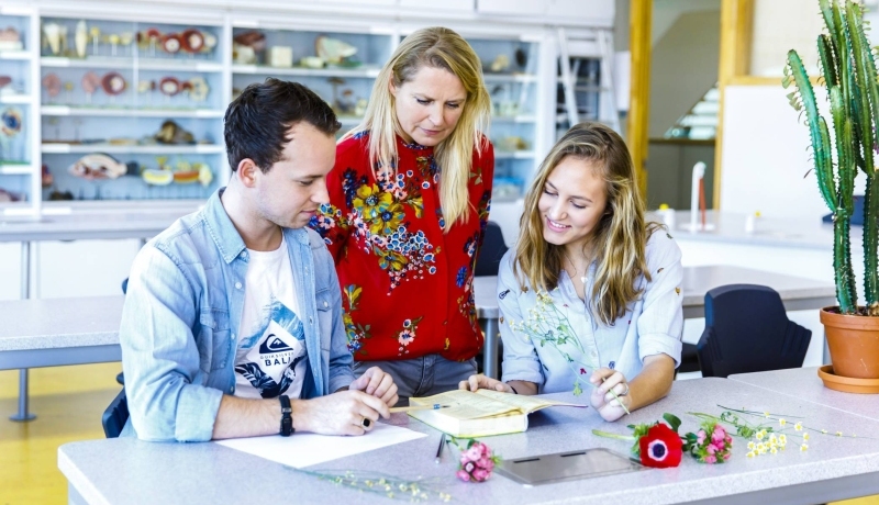 Docent maakt met studenten een opdracht in boek