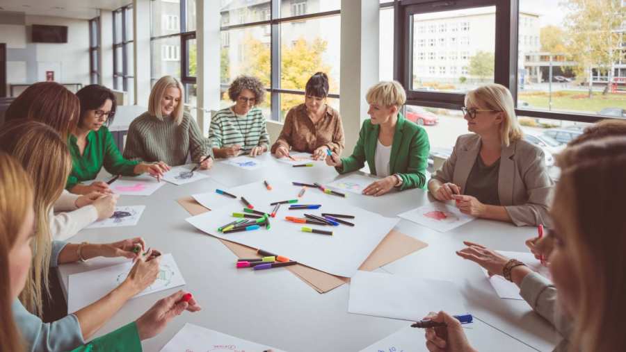 Een groep collega's zit een aan een grote tafel, met stiften en papieren. In een kantoorruimte.