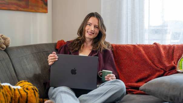 Student zit thuis op de bank aan het studeren met de laptop en een kop koffie