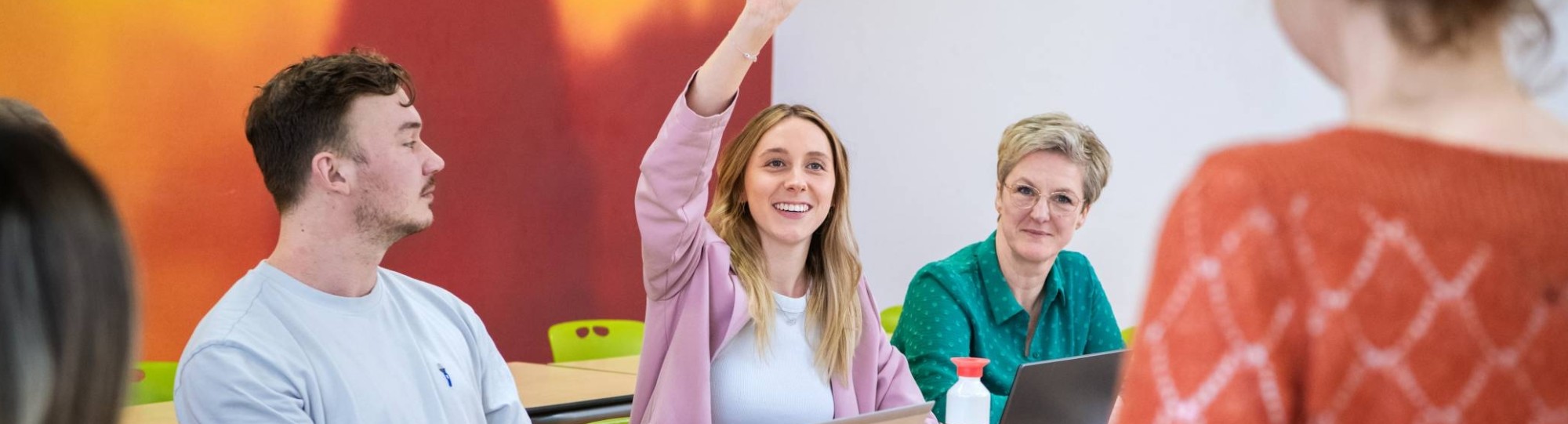 Drie master studentes zitten lachend aan tafel.