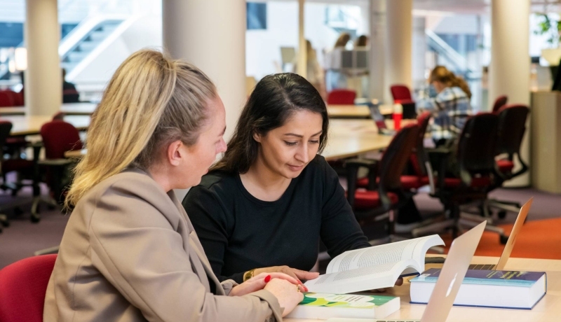 Twee studenten aan het werk in de bibliotheek en kijken naar een boek voor studie PMT deeltijd