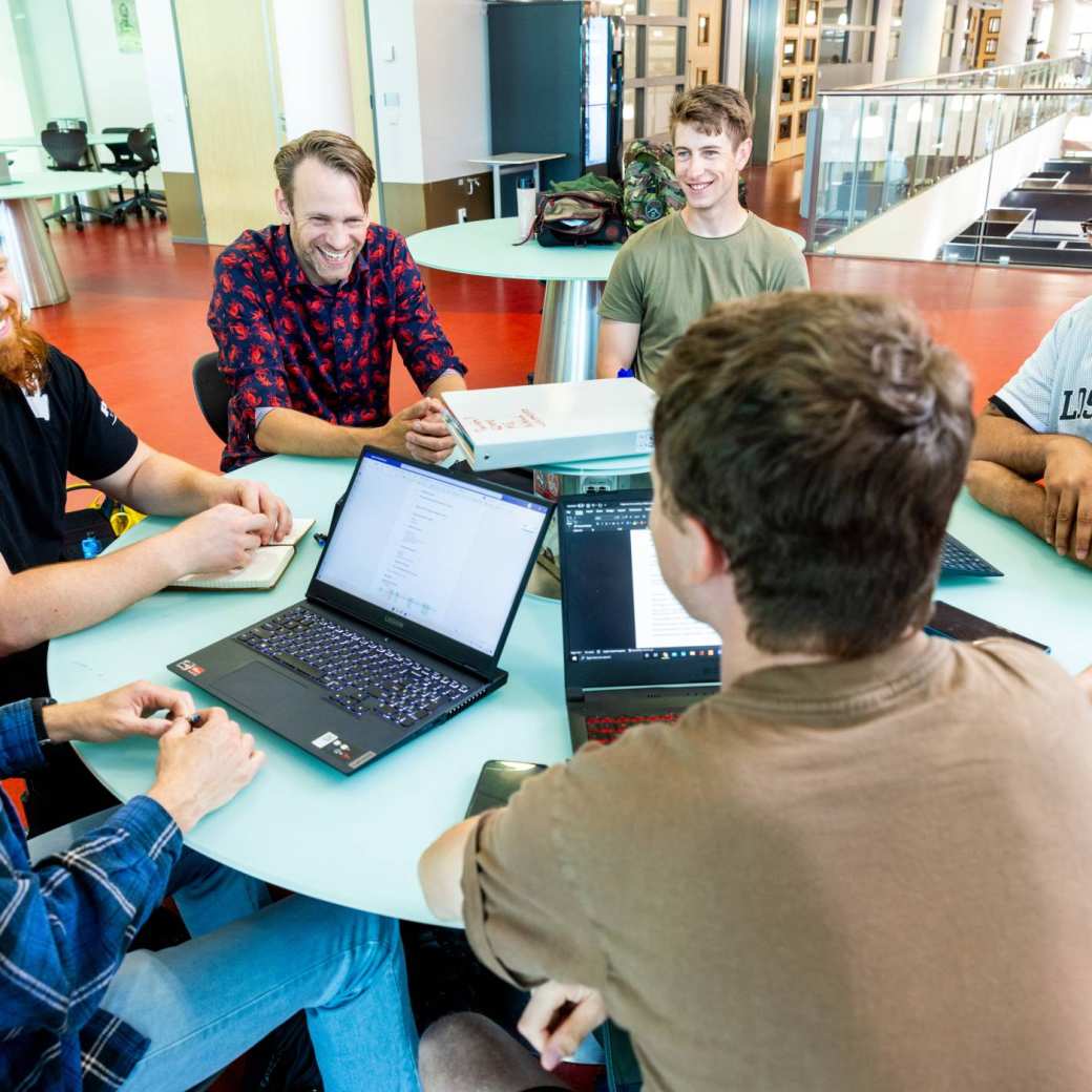 a group of engineering students -mechanical werktuigbouwkunde - working on a project together at a round table with laptops