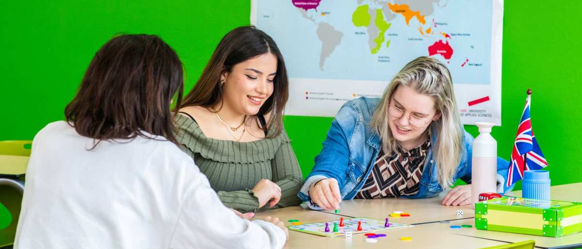 Drie studenten spelen in een lokaal waar de Engelse vlag hangt 'Mens, erger je niet!'