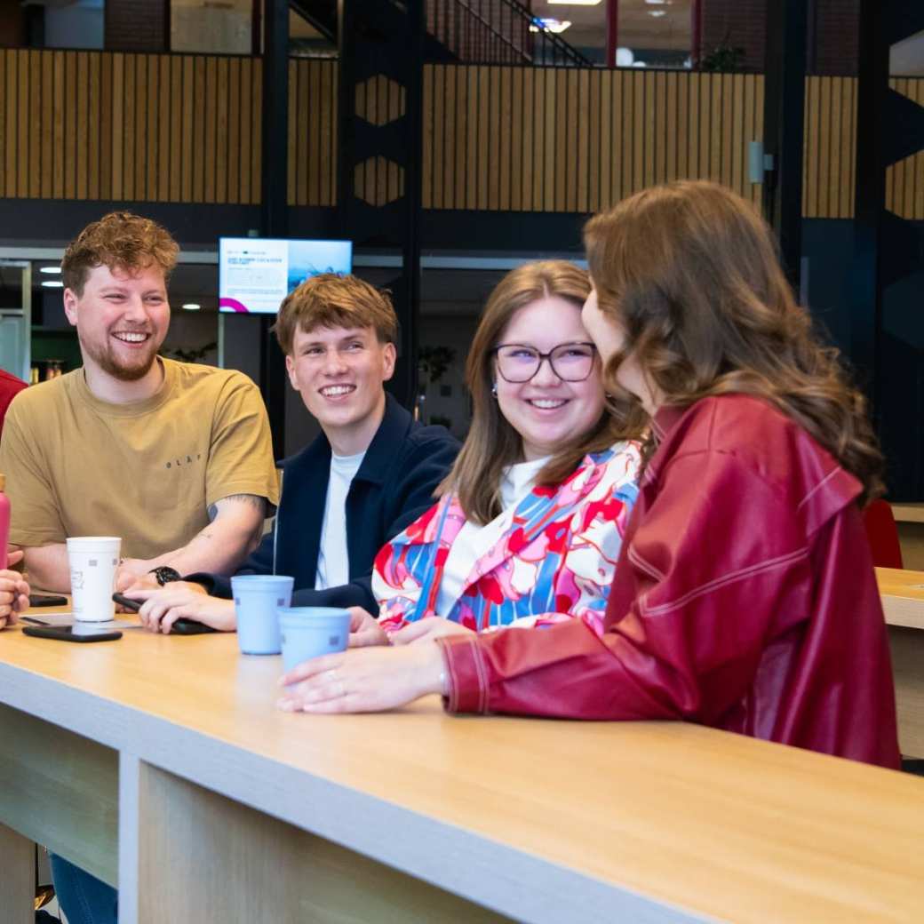 Studenten praten met elkaar aan de uitleenbalie van Ergotherapie met koffie en thee.