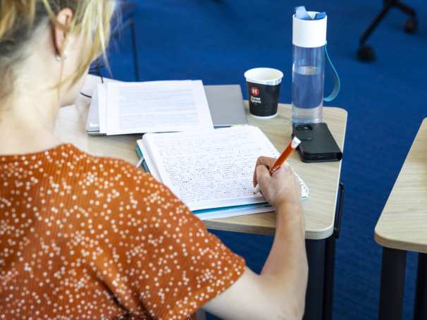 Student van de Master Social Work maakt aantekening met pen en papier.