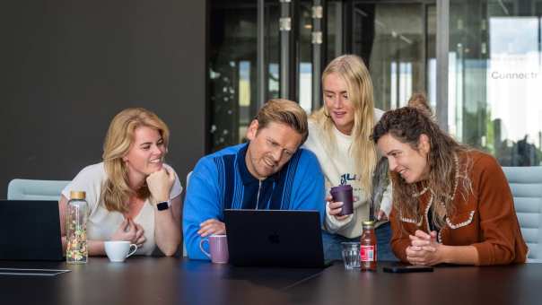 Groep studenten aan tafel kijkend naar laptop in overleg