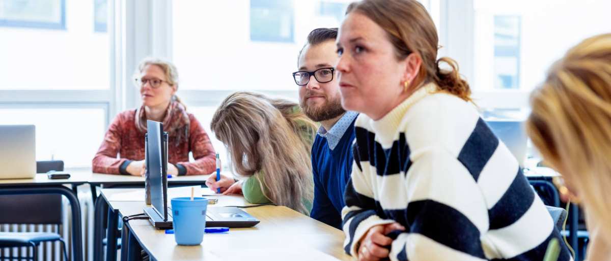 Vrouw met witte trui met zwarte strepen luistert naar presentatie. Op de groenewoudseweg, opleiding maag-, lever,- darmverpleegkundige.