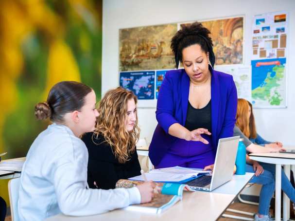 Angel Olatunji geeft staand uitleg bij een tafel met 2 middelbare scholieren van het Citadel College.