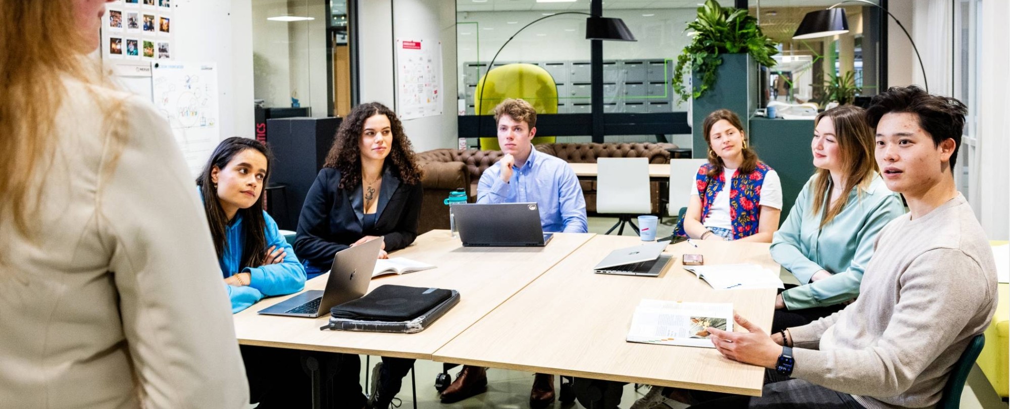 Bedrijfskunde voltijd studenten zitten in de studio aan een tafel en luisteren naar de docent