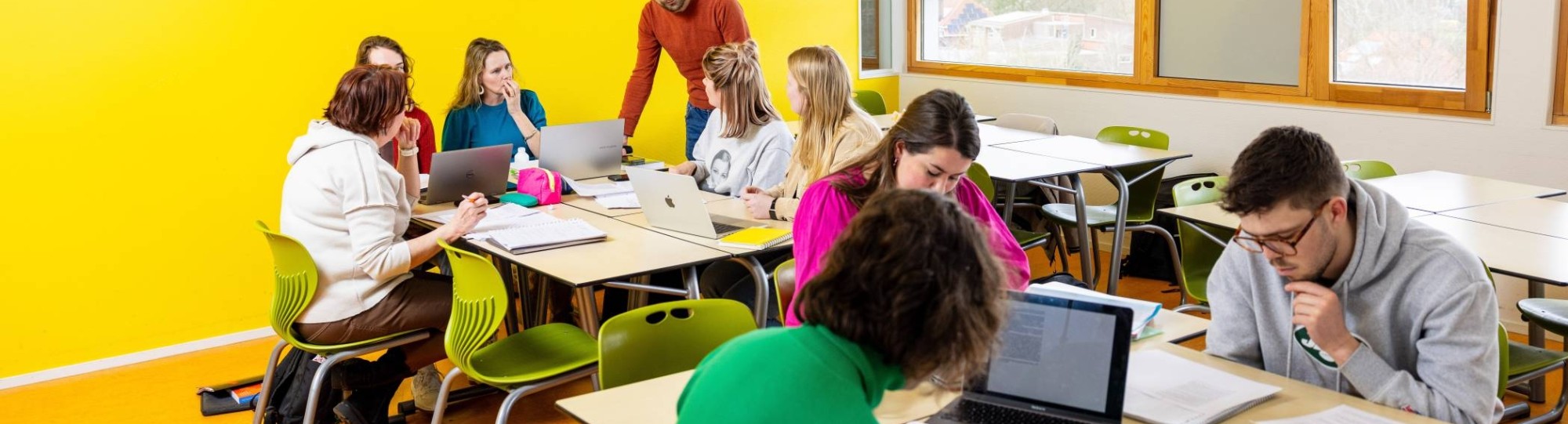 De docent loopt rond in het klaslokaal. De studenten zijn aan het werk.