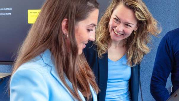 Een man en twee vrouwen staan met elkaar te kijken naar een laptop en een klaslokaal