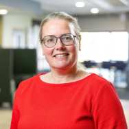 Haren naar achteren vast gestoken, brildragend. Rode trui