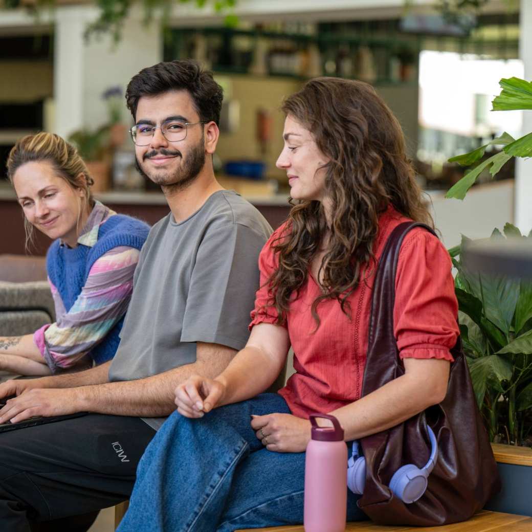 Drie studenten werken aan opdracht met laptop in de gang.
