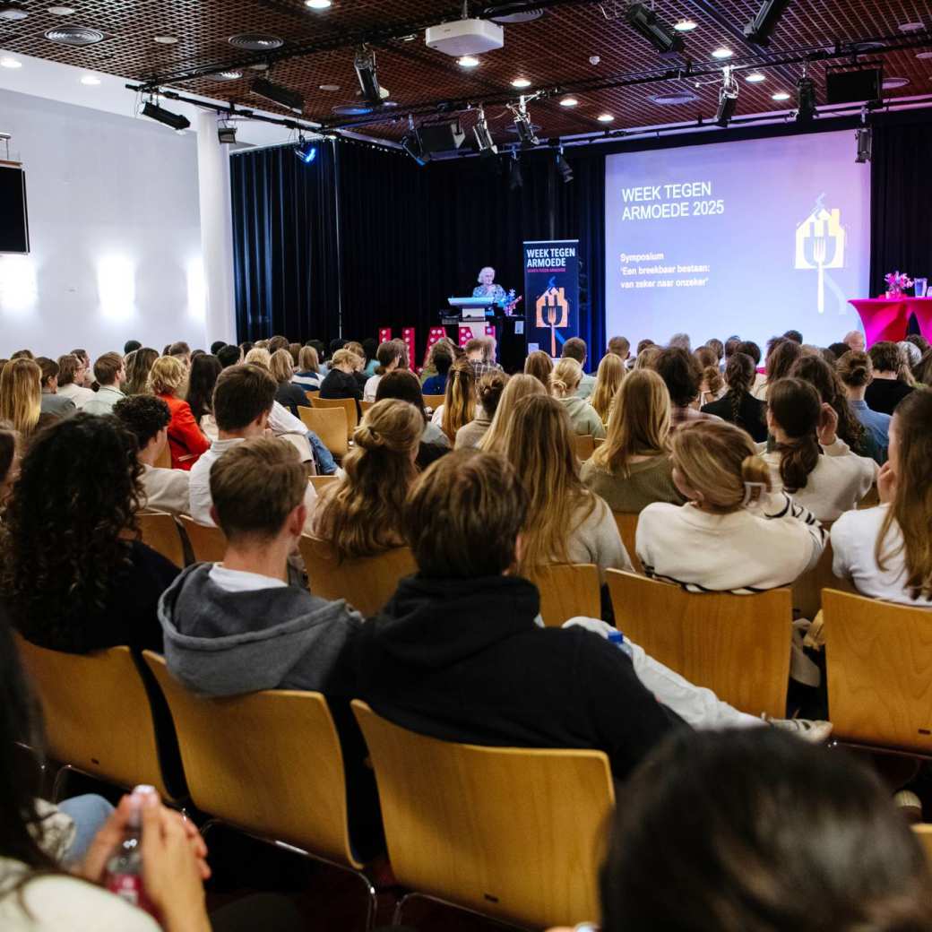 Volle zaal in Nijmegen met mensen in stoelen met voorraan een podium waar Yvonne de Haan, vrouw met blonde krullen, haar verhaal doet.