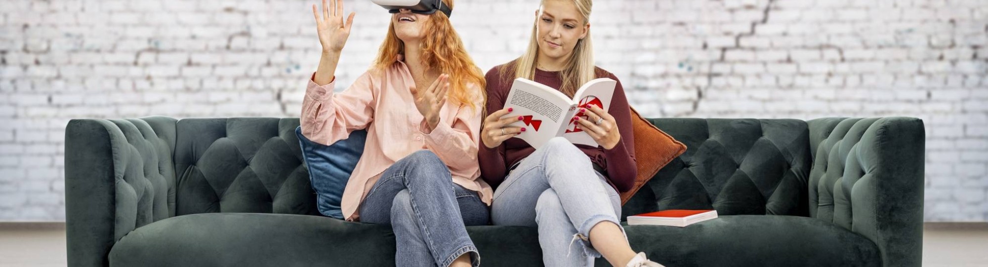 Een meid met vr-bril en een meid met een boek zitten samen op de bank