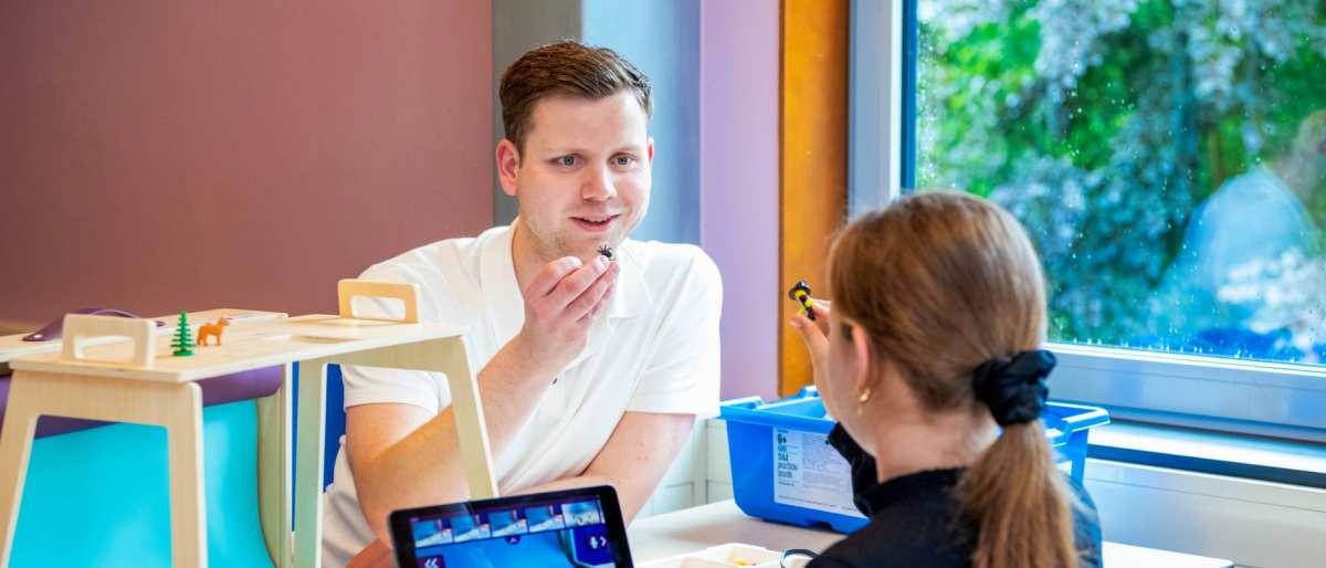 Een docent en kind houden iets in hun hand vast.
