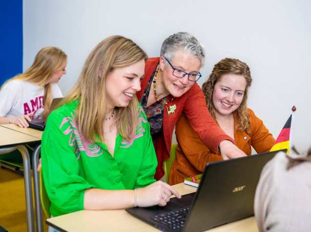 Lerarenopleider helpt twee studenten door iets aan te wijzen op de laptop die voor hun staat.