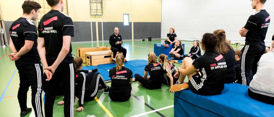 studenten krijgen uitleg van docent in sporthal.