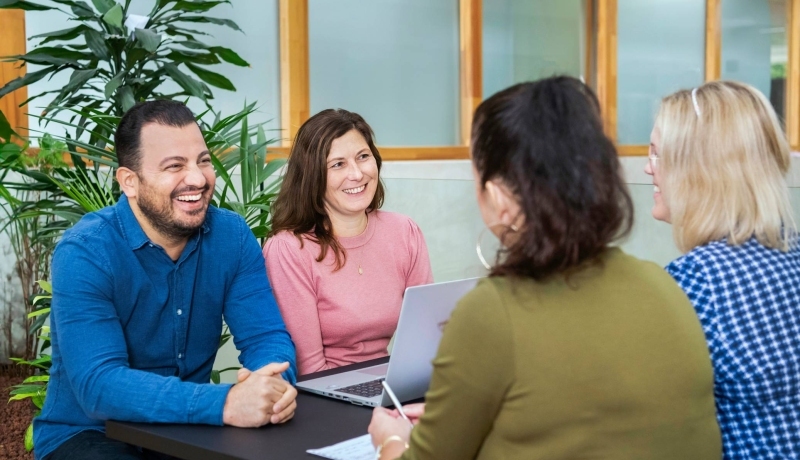 Drie master studentes zitten lachend aan tafel.