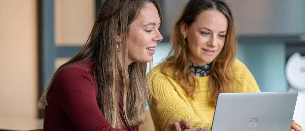 2 studenten kijken lachend samen naar een laptop.