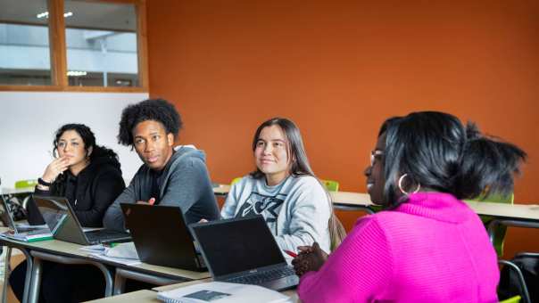 vier masterstudenten aan tafel en kijken naar de docent