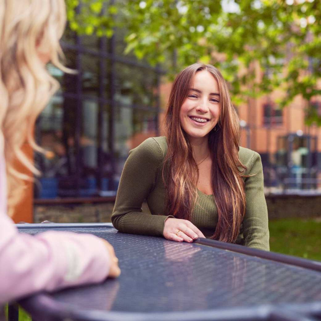 werving voltijd campagne, twee studentes in gesprek aan een picnictafel in de binnentuin.