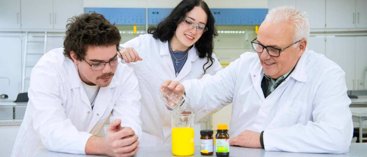 Twee studenten zijn met docent in het lab een proef aan het uitvoeren.
