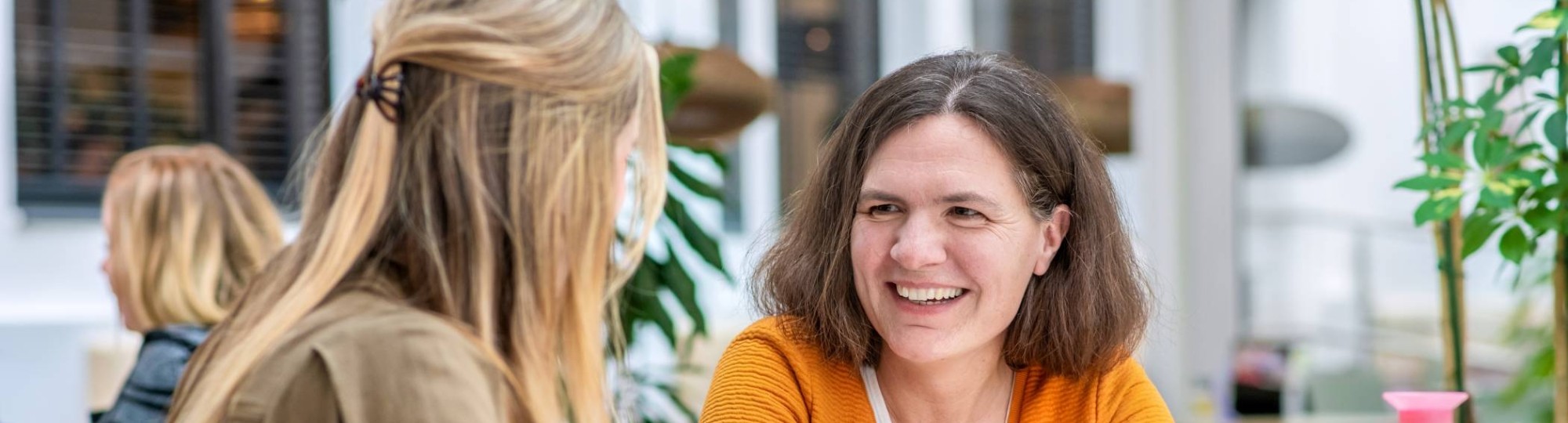 Vrouw in oranje trui lacht naar medestudent.