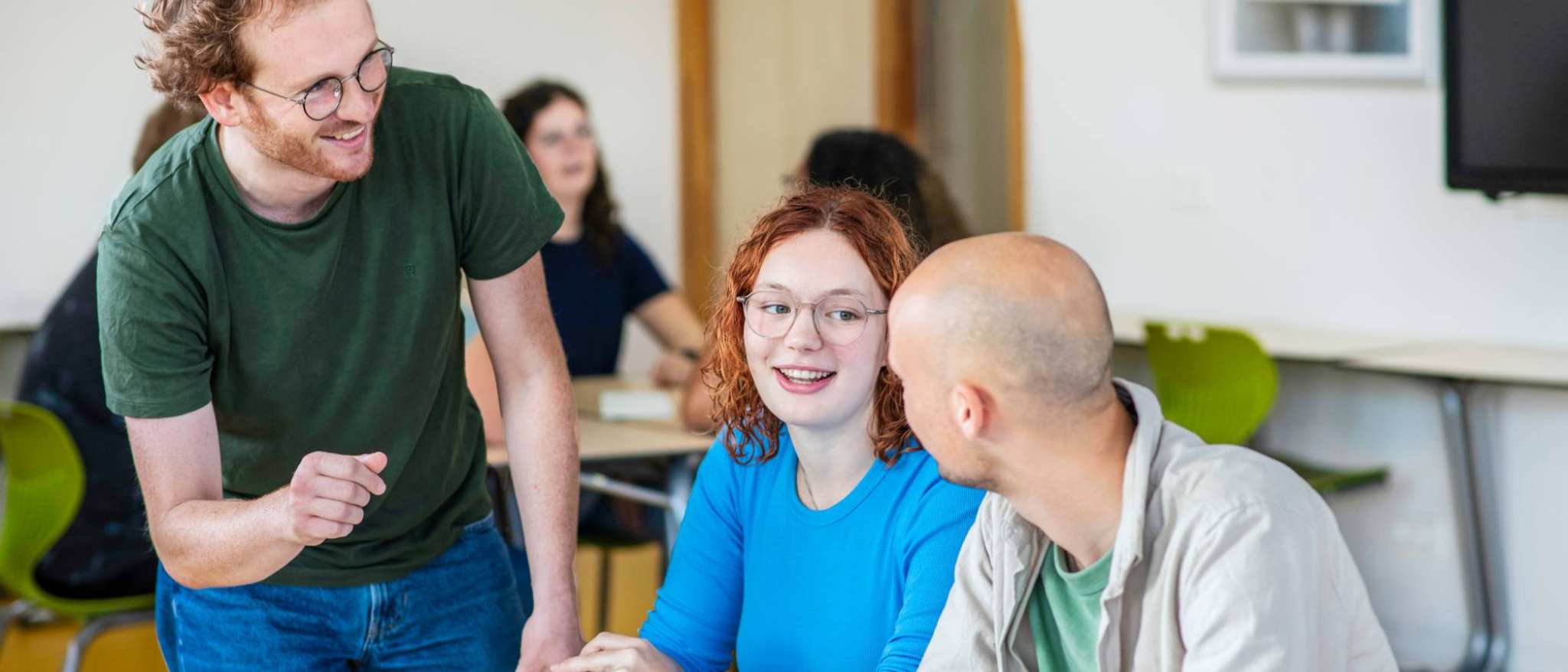 Leraar Wiskunde luistert lachend naar zijn twee studenten die iets zeggen tegen hem