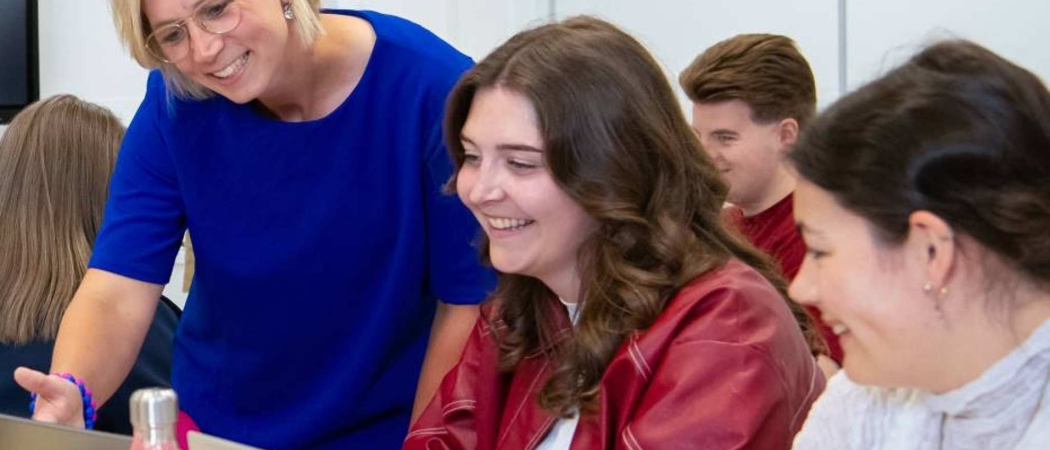 Docnt geeft uitleg aan studenten in een leslokaal die achter een laptop zitten