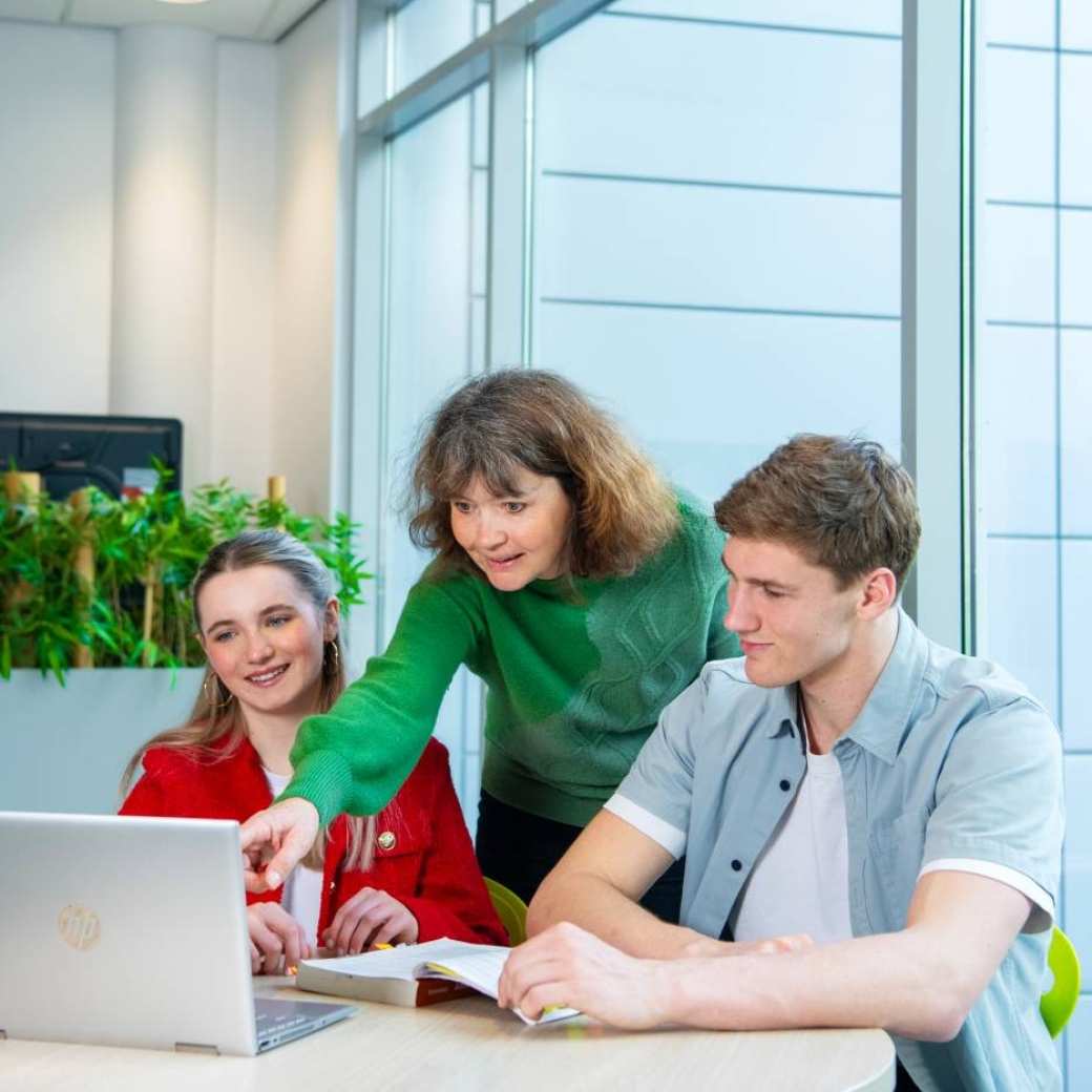 Twee studenten van hbo human resource management in overleg, een docent wijst naar de laptop