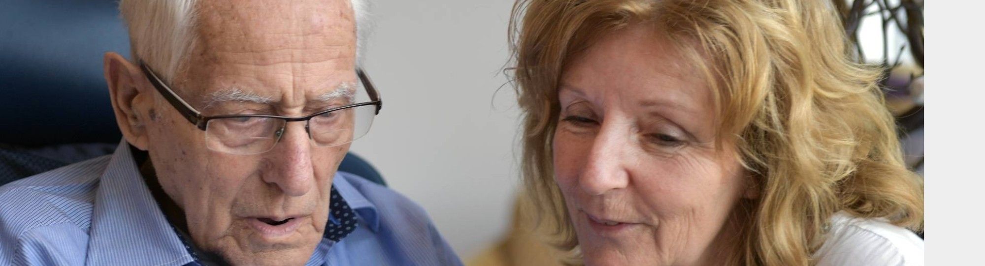 medewerkster toont foto’s op een tablet aan een bewoner van het verpleeghuis