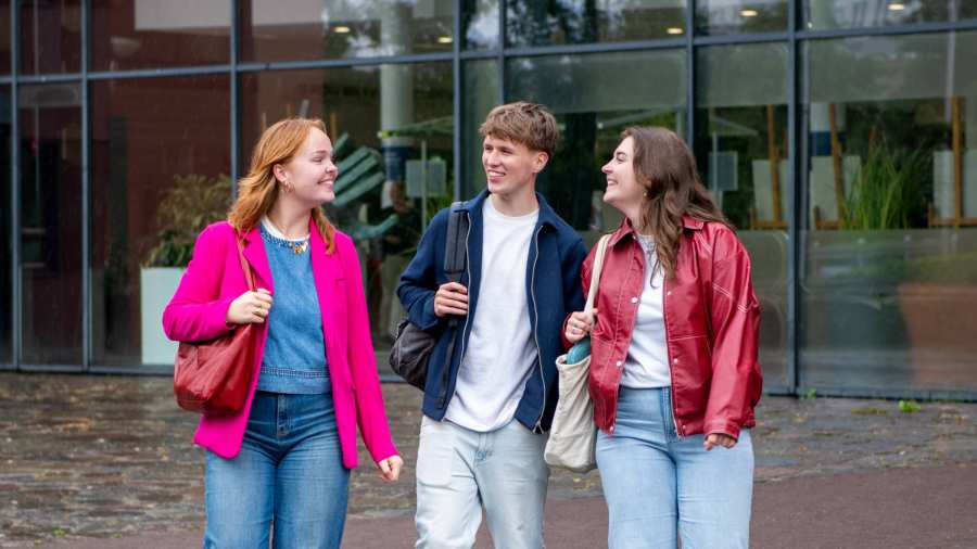 2 meiden en een jongen kijken elkaar aan en lopen bij de hoofdingang van de HAN campus in Nijmegen