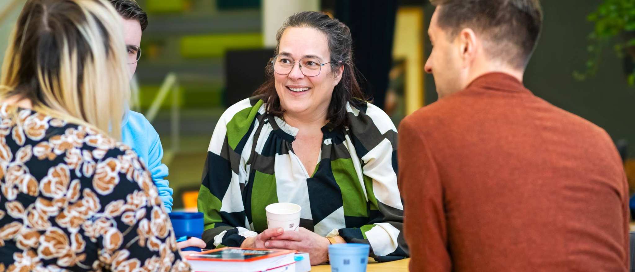 Een vrouw lacht tijdens een gesprek met andere studenten.