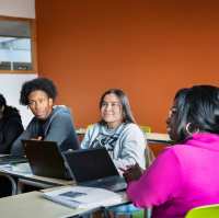 vier masterstudenten aan tafel en kijken naar de docent