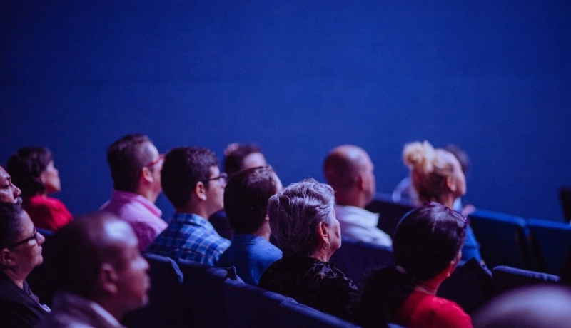 Een beeld van mensen die in een zaal zitten te luisteren