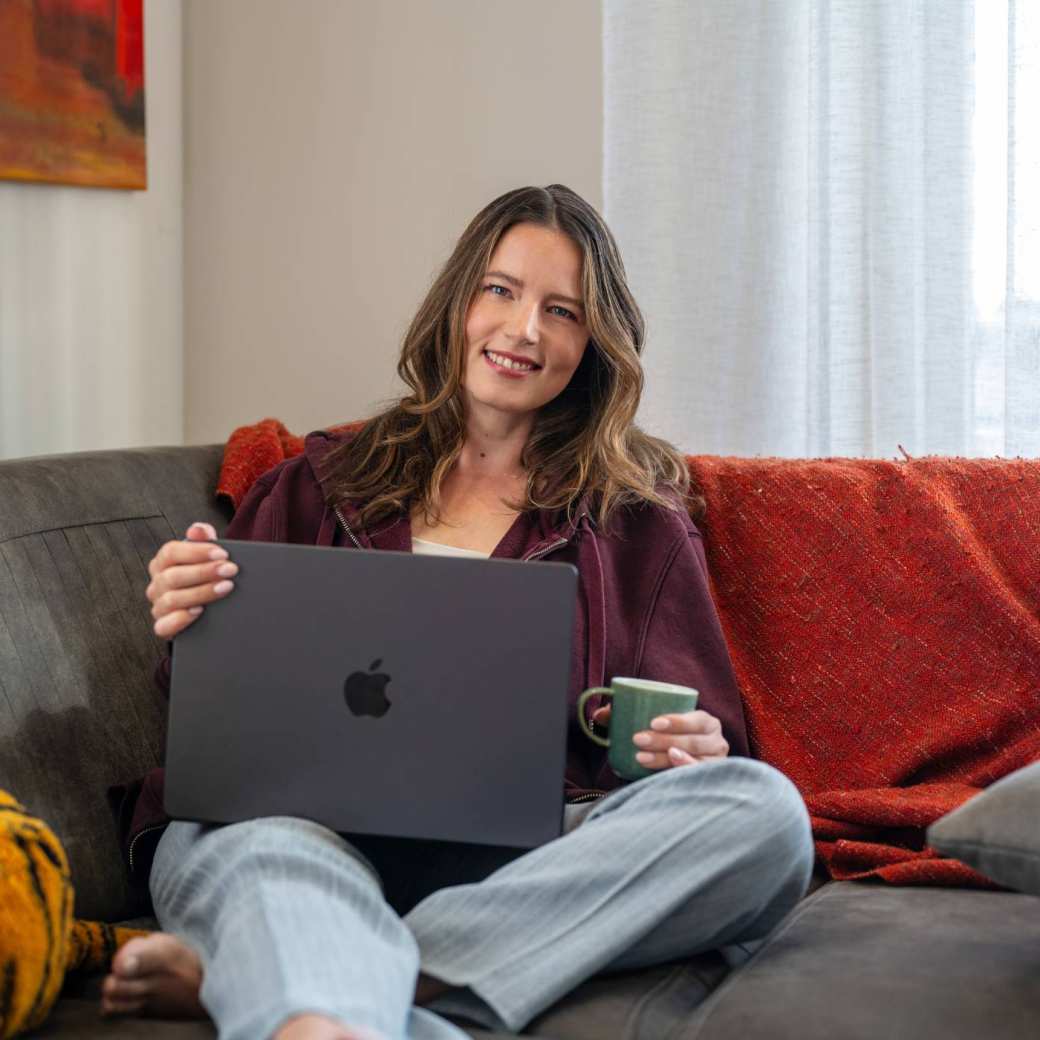 Student zit thuis op de bank aan het studeren met de laptop en een kop koffie