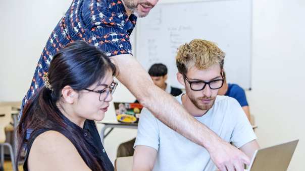 Docent geeft persoonlijke uitleg aan studenten MHV achter laptop