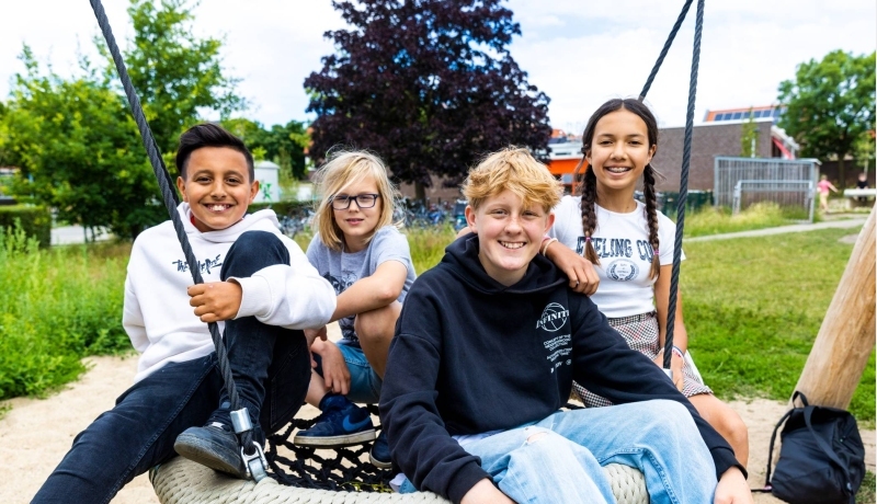 Vier leerlingen zitten buiten op een schommel. Foto van de opleiding leraar basisonderwijs