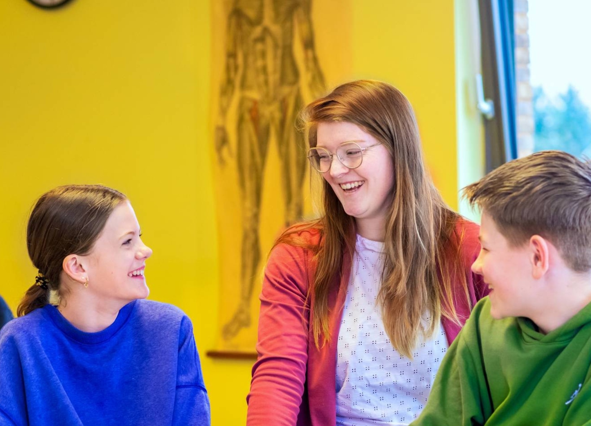 Fotoshoot op het Citadel 2024. De docente lacht met 2 scholieren in de klas.