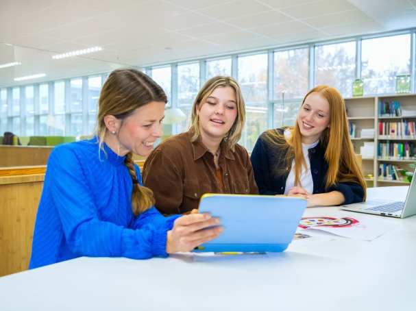 Drie mensen zitten aan een tafel met een tablet en een laptop en lachen.