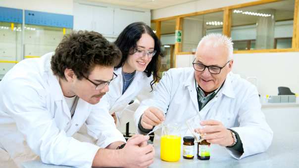 Twee studenten in een labjas kijken aandachtig naar een reageerbuisje.
