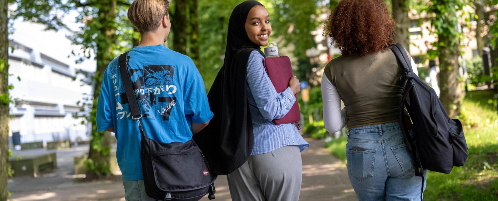 Studenten lopen buiten van K33 naar LvS10, pad bij bomen, campusterrein.