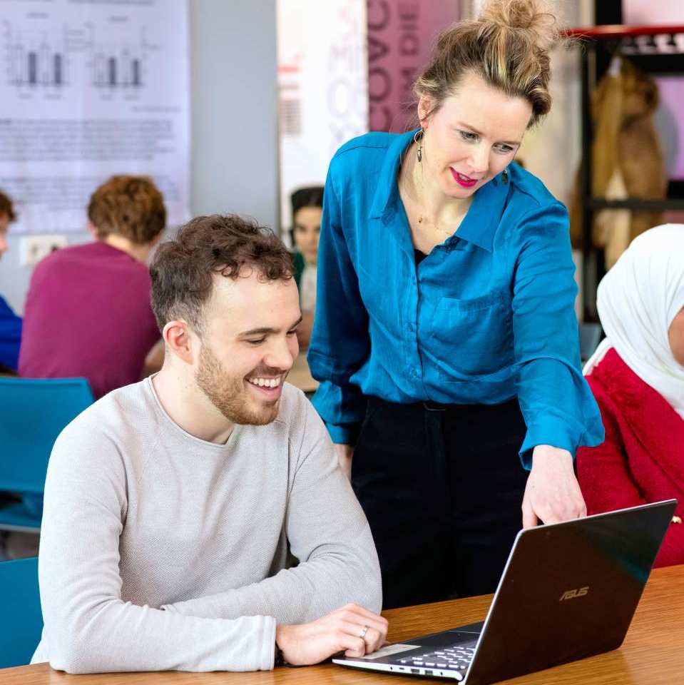 Docent en student kijken samen op laptop