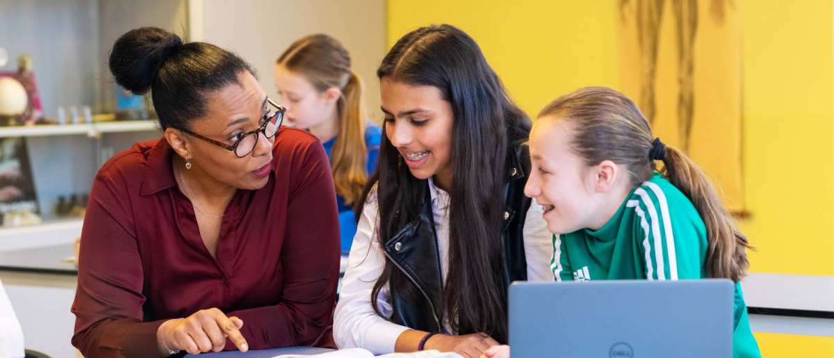 Docenten Claudine Laclé geeft uitleg aan 2 leerlingen en wijst in het schrift voor ze op tafel op het Citadel College.