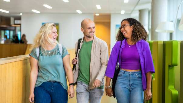 Drie studenten Leraar Wiskunde lopen lachend naast elkaar op de gang in de school