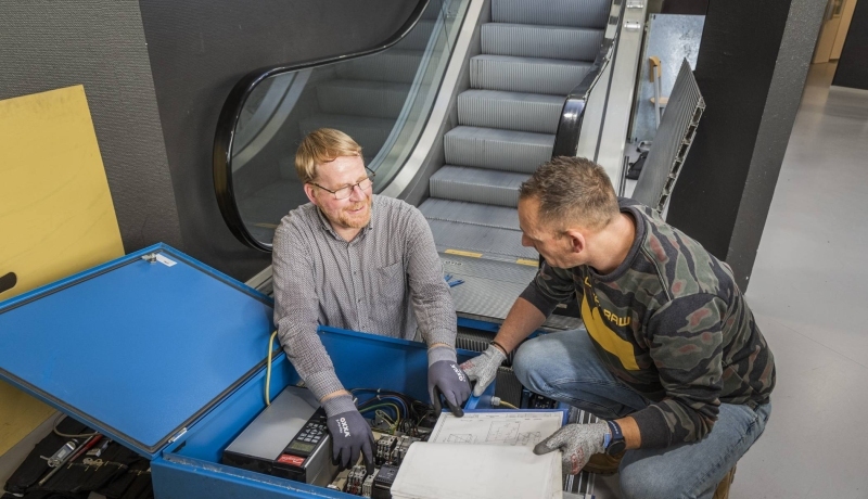 Twee cursisten voor het praktijkexamen BOEI in overleg voor een roltrap.