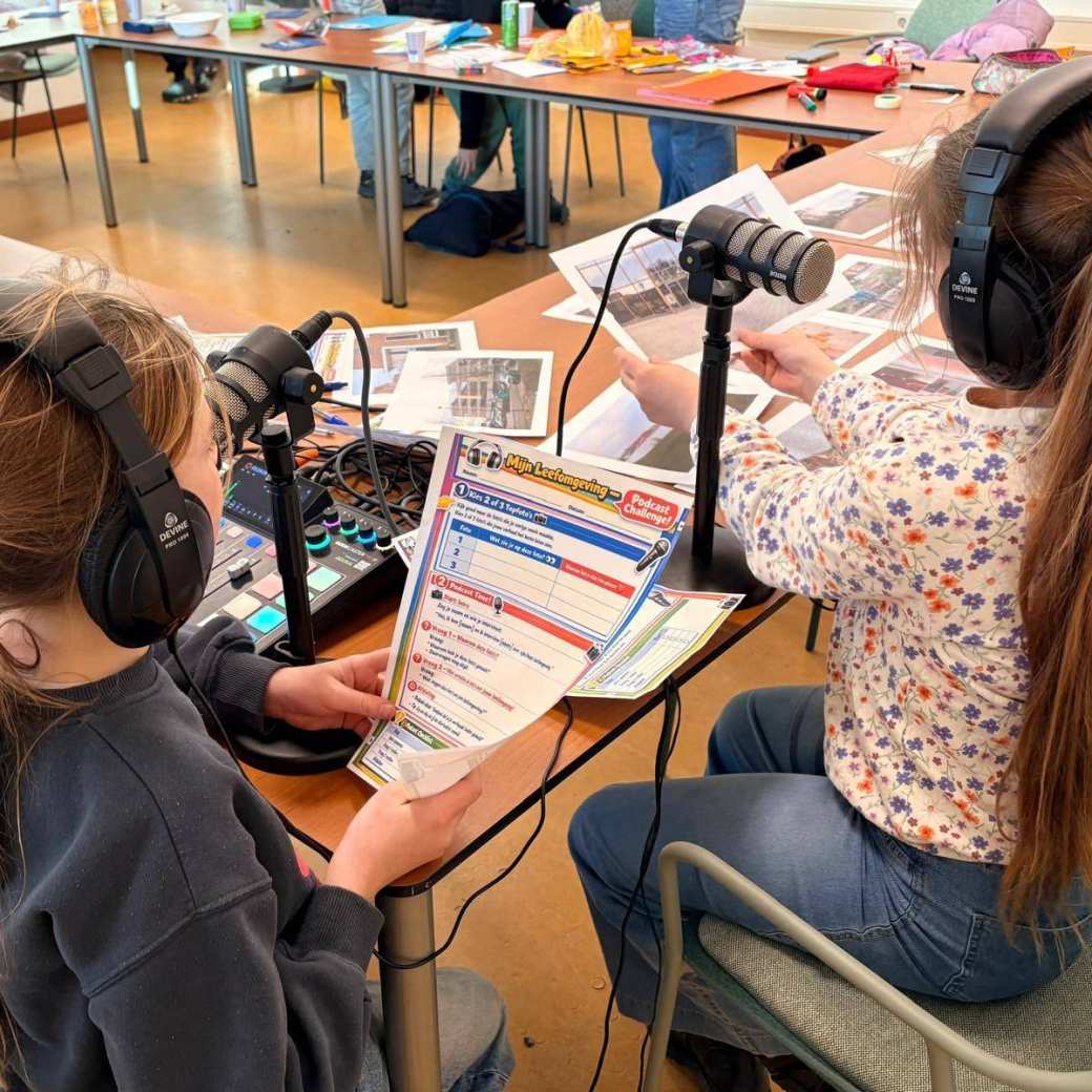 Foto van twee meisjes (met koptelefoons en foto's uit hun buurt) in gesprek met professionals over hun leefomgeving
