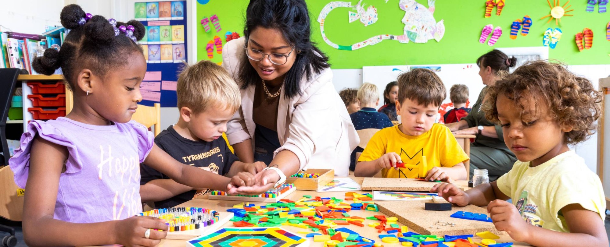 De kinderen in de klas leggen een puzzel en de lerares van de opleiding leraar basisonderwijs helpt hen hierbij.