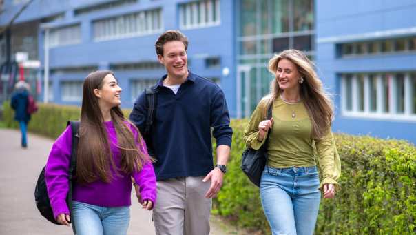Drie studenten van Learning and Development in Organisations voltijd lopen lachend voor het HAN gebouw in Nijmegen.